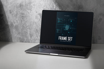 A dark gray laptop sits open on a white surface against a textured gray wall, displaying a digital cover titled 'FRAME SET' with a futuristic blue interface and a face graphic on the screen.